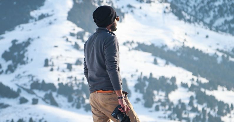 Adventure - Man Wearing Gray Long-sleeved Shirt and Brown Shorts Holding Black Dslr Camera on Mountain