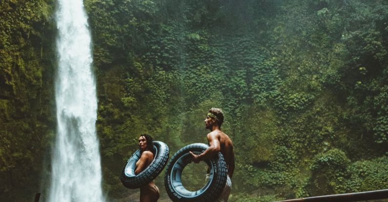 Adventure - Two Person Carrying Black Inflatable Pool Float on Brown Wooden Bridge Near Waterfalls