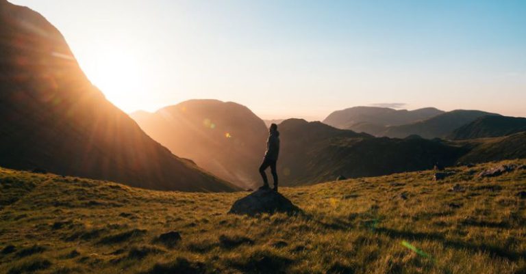 Hiking - Silhouette Photography of Person Standing on Green Grass in Front of Mountains during Golden Hour